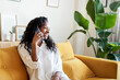 © CarlosBarquero - Happy African American woman on a call sitting on a sofa in living room at home