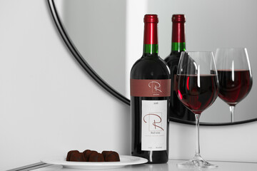 Sticker - Bottle and glass of red wine with chocolate candies on table near mirror