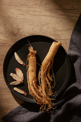  A black plate contains fresh ginseng, some ginseng slices with black silk.