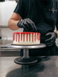 cake designer decorating a red drip cake with berries on the top