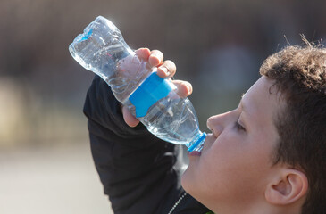 The boy drinks water from a plastic bottle.