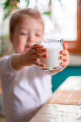 Selective focus of glass with milk. Close-up of glass of milk in the hands of a cute girl in the blurry background