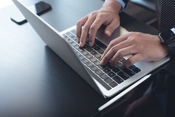 Wall Mural - Businessman in black suit busy working on new project with notebook computer, digital tablet on table at office. Business man standing at desk, hands typing on notebook computer