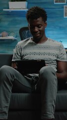 Poster - Vertical video: Modern adult looking at digital tablet for remote work at home. Person working on business project with gadget and browsing internet. Young man using technology and networking