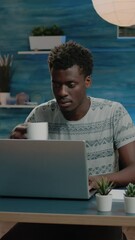 Poster - Vertical video: Freelance employee working from home on laptop and typing. Man doing remote corporate business work with technology while drinking cup of coffee. Networking entrepreneur with notebook