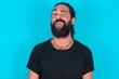 © Roquillo - young bearded man wearing black T-shirt over blue studio background sticking tongue out happy with funny expression. Emotion concept.