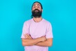 © Roquillo - Serious pensive young bearded man wearing violet T-shirt over blue studio background feels like cool confident entrepreneur cross hands.