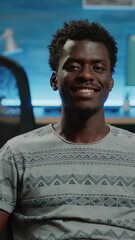 Poster - Vertical video: Close up of adult looking at camera and smiling on couch. Portrait of man smiling after doing remote work for freelance business. POV of cheerful person at home enjoying free time
