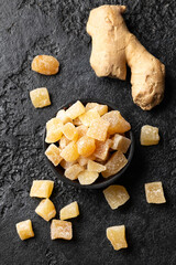 Wall Mural - Sweet and spicy candied ginger in black bowl on dark stone background. Top view