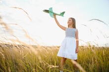 Happy Girl Runs With A Toy Airplane On A Field In The Sunset Light. Children Play Toy Airplane. Teenager Dreams Of Flying And Becoming A Pilot. Girl Wants To Become A Pilot And Astronaut. Slow Motion.