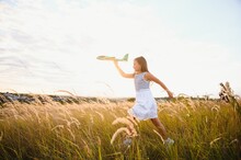 Happy Girl Runs With A Toy Airplane On A Field In The Sunset Light. Children Play Toy Airplane. Teenager Dreams Of Flying And Becoming A Pilot. Girl Wants To Become A Pilot And Astronaut. Slow Motion.