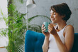© ViDi Studio - Close up side view young woman wear white tank shirt drink tea coffee sniff sit on blue sofa stay at home flat rest relax spend free spare time in living room indoors grey wall People lounge concept.