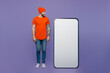Full body young fun man wear red hat t-shirt stand look at near big huge blank screen mobile cell phone workspace mockup area isolated on plain pastel light purple background People lifestyle concept.