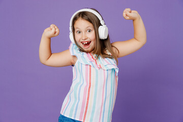 Little smiling cheerful kid child girl 5-6 years old wearing striped dress headphones listen music dance isolated on plain pastel light purple background. Mother's Day love family lifestyle concept.