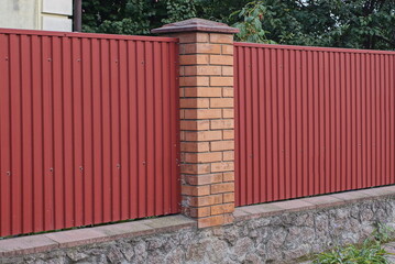 Poster - long fence wall made of metal and red bricks on a gray concrete foundation in green grass