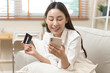 © Pormezz - Happy Asian young woman using mobile phone shopping online and pay via credit card to get cashback bonus.