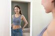 © Pormezz - Asian woman wearing her old pant before loss weight looking reflection in the mirror and feeling joyful with her body after diet success