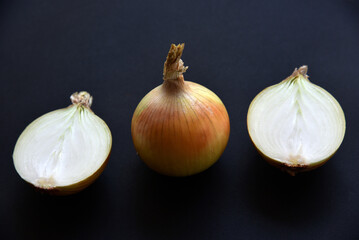 Wall Mural - Onion cut in half and whole on a black background. Delicious bulbs close-up.