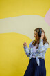 young woman in the summer outdoors listening to music in headphones and dancing against the background of a colored wall