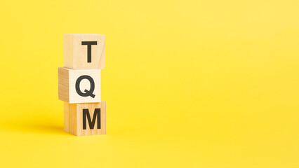 TQM - Total Quality Management - text on wooden block with yellow background