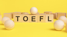 Text TOEFL On Wooden Cubes. Bright Yellow Surface. Wooden Sphere Balls Among The Wood Cubes, Different And Position In Niche Market Concept. TOEFL - Test Of English As A Foreign Language