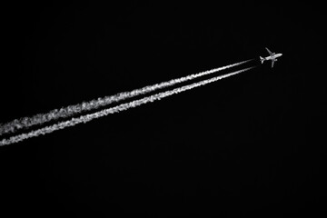 Twin-engined jetliner with contrails flying in black sky