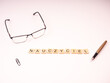 Nauczyciel - napis z drewnianych literek na białym tle, okulary, pióro 