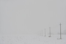 Poles With High-voltage Wires Extending Into The Distance In A Snowy Fog