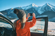Woman travel exploring, enjoying the view of the mountains, landscape, lifestyle concept winter vacation outdoors. Female with mobile phone standing near the car in sunny day.