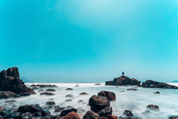 moon lighting over the sea and rocks on the coast at night with a silhouette in the background