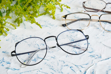 Wall Mural - Woman's eyeglasses and little yellow flowers branches on textured background. Flat lay