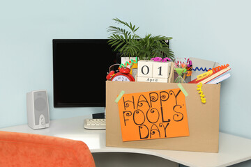 Wall Mural - Box with different items and words Happy Fool's Day at workplace in office