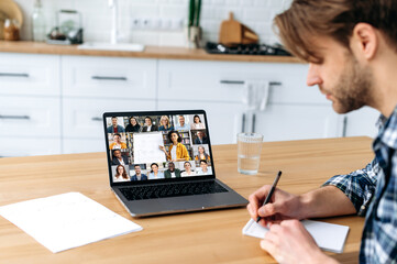 Sticker - Online education. Side view of a smart caucasian male student and group of multiracial people on a laptop screen. Clever guy listening to an online lecture, takes notes, gain knowledge distantly