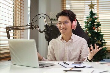 Man vlogger in headphone podcast using microphone and laptop broadcasting live audio podcast at home studio.