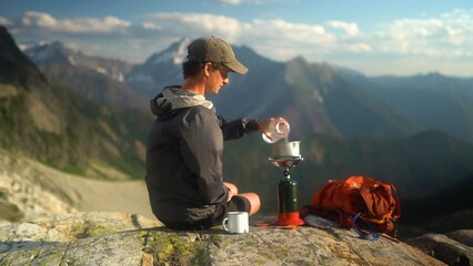 young caucasian man on camping trip pours water into pot to boil for morning coffee