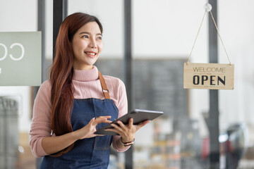 Portrait of a friendly young asian business woman barista wearing apron and standing with her arms crossed at the door of a trendy cafe, open sign barista SME entrepreneur seller concept