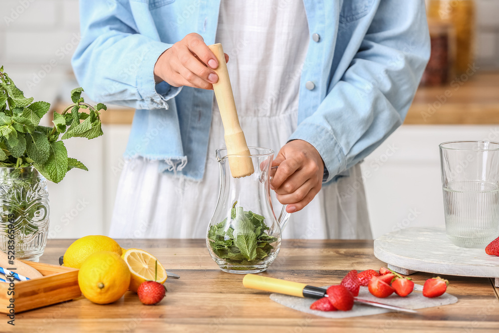 Woman preparing tasty strawberry lemonade on kitchen counter