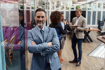 Wall Mural - Portrait of mature businessman standing in modern office on colleagues background