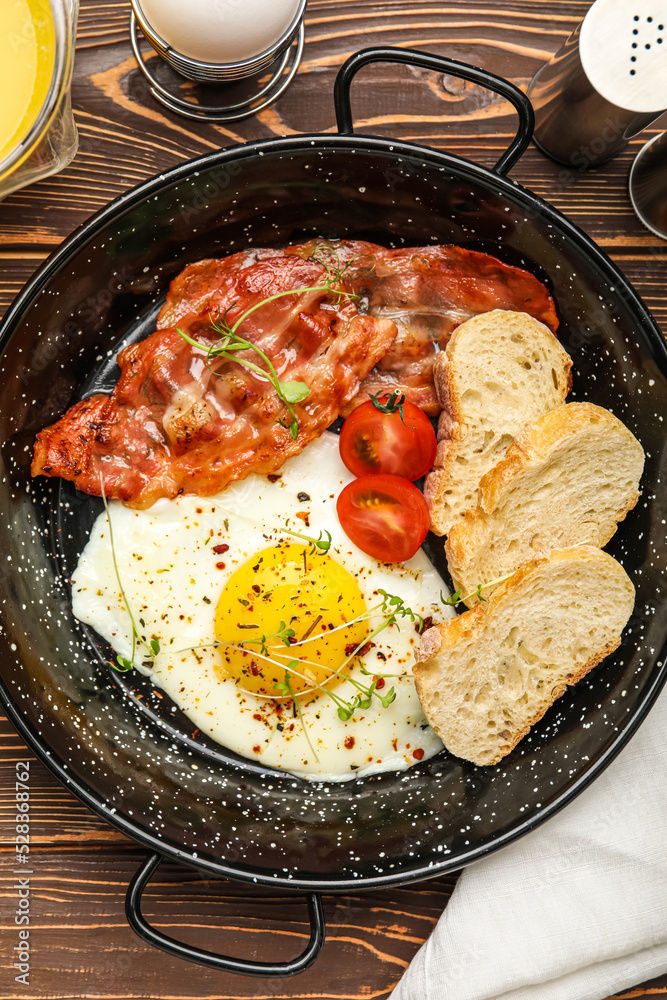 Frying pan with tasty fried egg, bacon and bread on wooden table, closeup