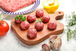 Cutting board with raw meat balls and herbs on light background