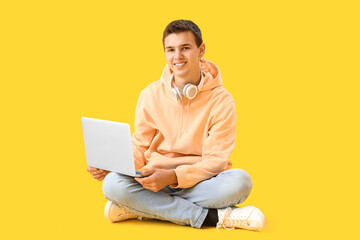 Wall Mural - Teenage boy with headphones and laptop on yellow background