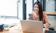 © NAMPIX - Happy young asian businesswoman using mobile phone, standing at desk with laptop computer.