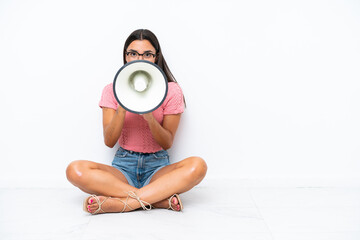 Wall Mural - Young caucasian woman sitting on the floor isolated on white background shouting through a megaphone