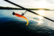 A fragment of a spinning rod and a silicone bait against the background of the river and the sun's rays. Fishing for predatory fish in the summer. Foreground
