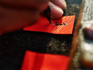 Closeup shot of the process of writing Chinese letters on a red paper to sell