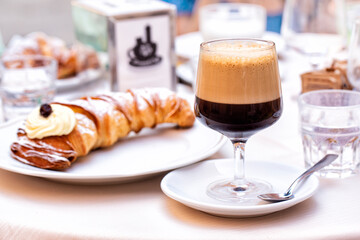 Italian breakfast table in a cafe. Caffè shakerato in a tall glass. Cold shaked coffee with a foam made with ice. A sfogliatella or lobster tail,  shell-shaped pastry with cream. Italy.