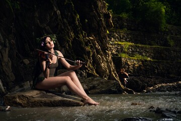 Wall Mural - Pretty caucasian girl in brown short dress with a flowers crown sitting on a rock in the park river