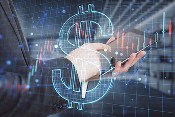 Poster - businessman hand pointing at tablet with creative glowing dollar sign hologram with forex chart on blurry office interior background. 