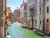 Fototapeta Uliczki - View on the narrow cozy streets of the canals with parked boats in Venice, Italy. Architecture and landmark of Venice.
