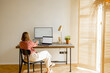 © rh2010 - Woman works on computers while sitting by a cozy workplace in sunny living room at home. View from the backside. Concept of remote work from home office. Mockup image